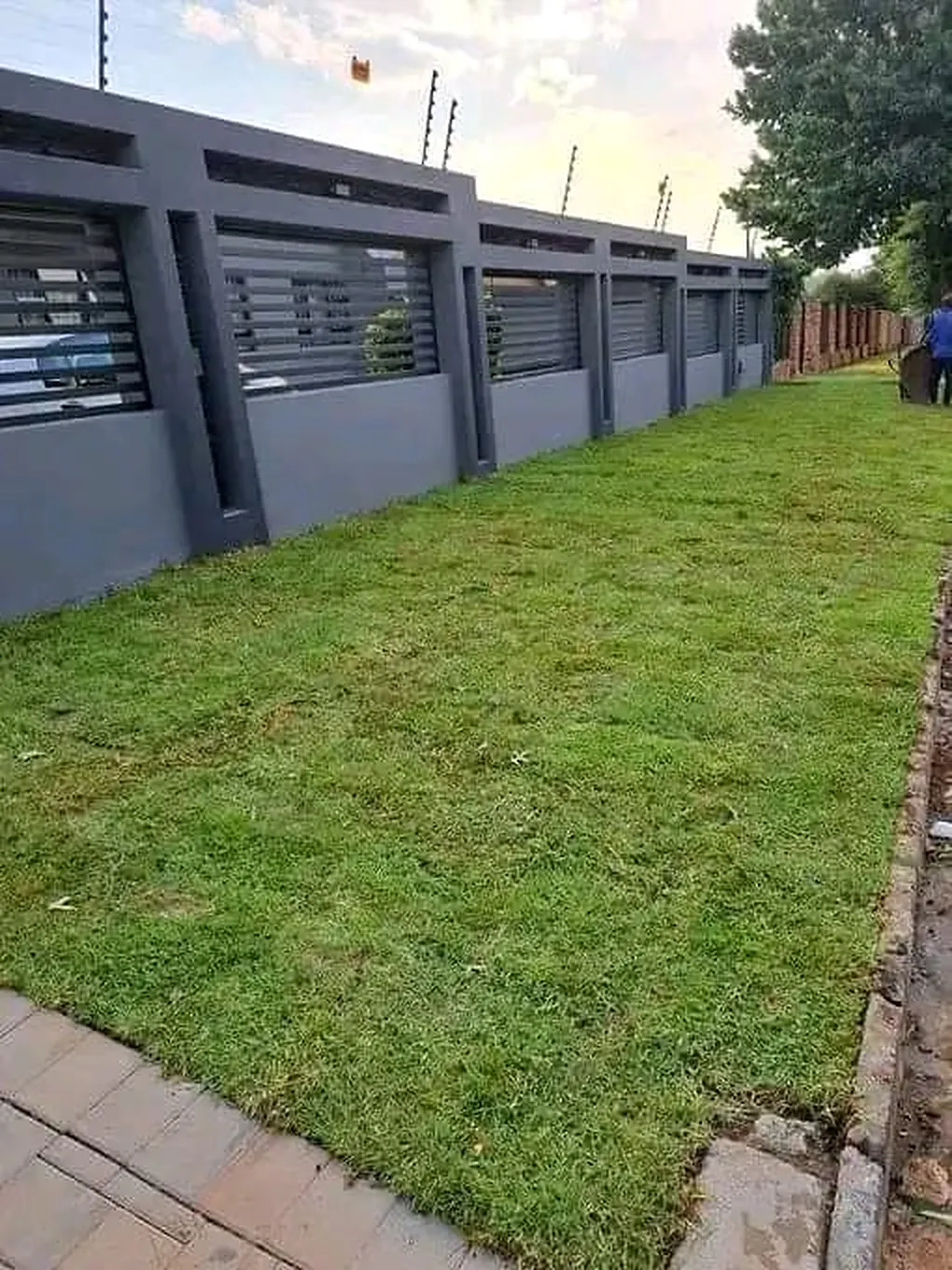 A strip of new lawn running along a modern boundary wall and paved edge