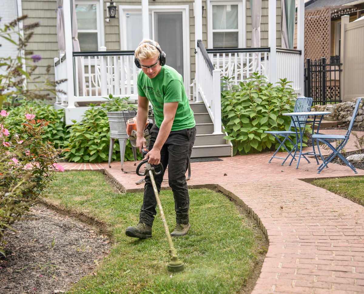 A landscaper edging a lawn along a brick garden path